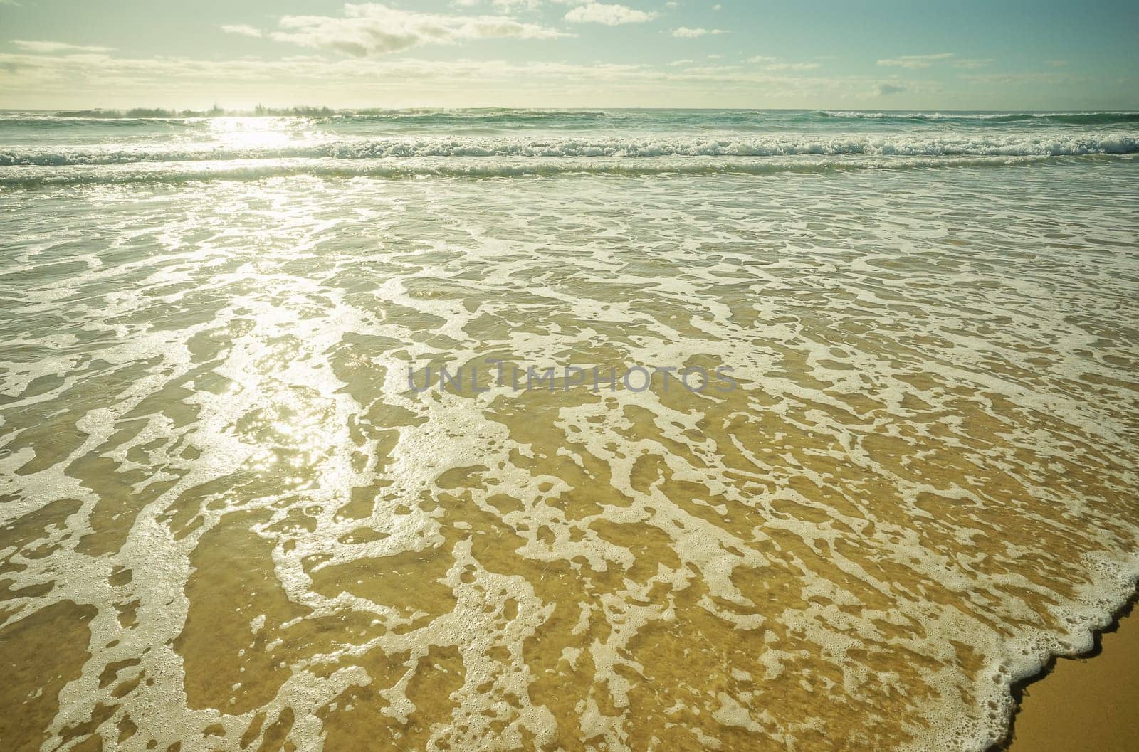 Foamy white wash as waves break and roll across the sandy beach. Empty background concept with copy space for seaside holiday, vacation, honeymoon, relaxation, inspiration, meditation, relaxing