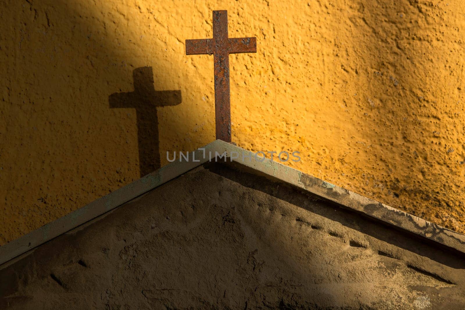 Cross on a tombstone at a yellow wall in a sunbeam