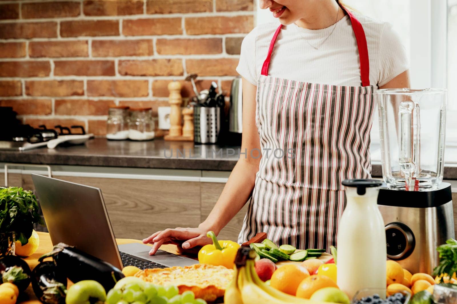 Woman using laptop at home kitchen. Girl touching touchpad with hand, searching for a recipe. Chef using pc, online food shopping on computer. Delivery app ads concept, cook book or diet plan recipes