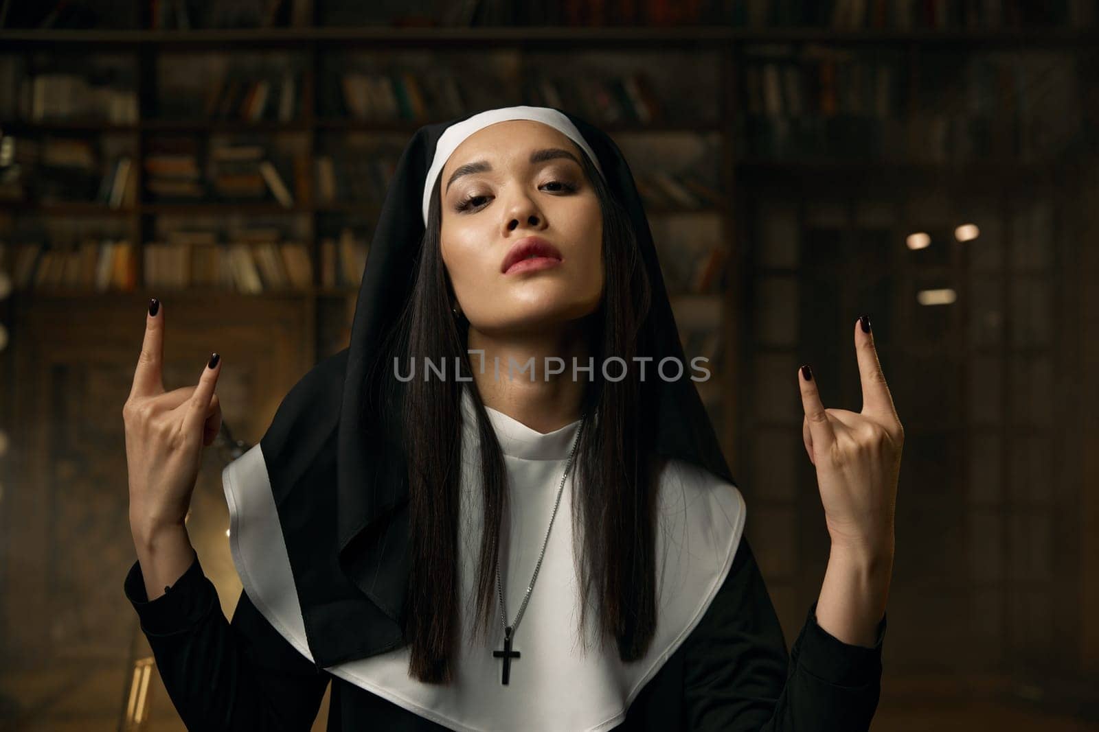 Portrait of passionate catholic nun gesturing heavy metal rock symbol with two hands. Rock-and-roll music, religion and desire concept