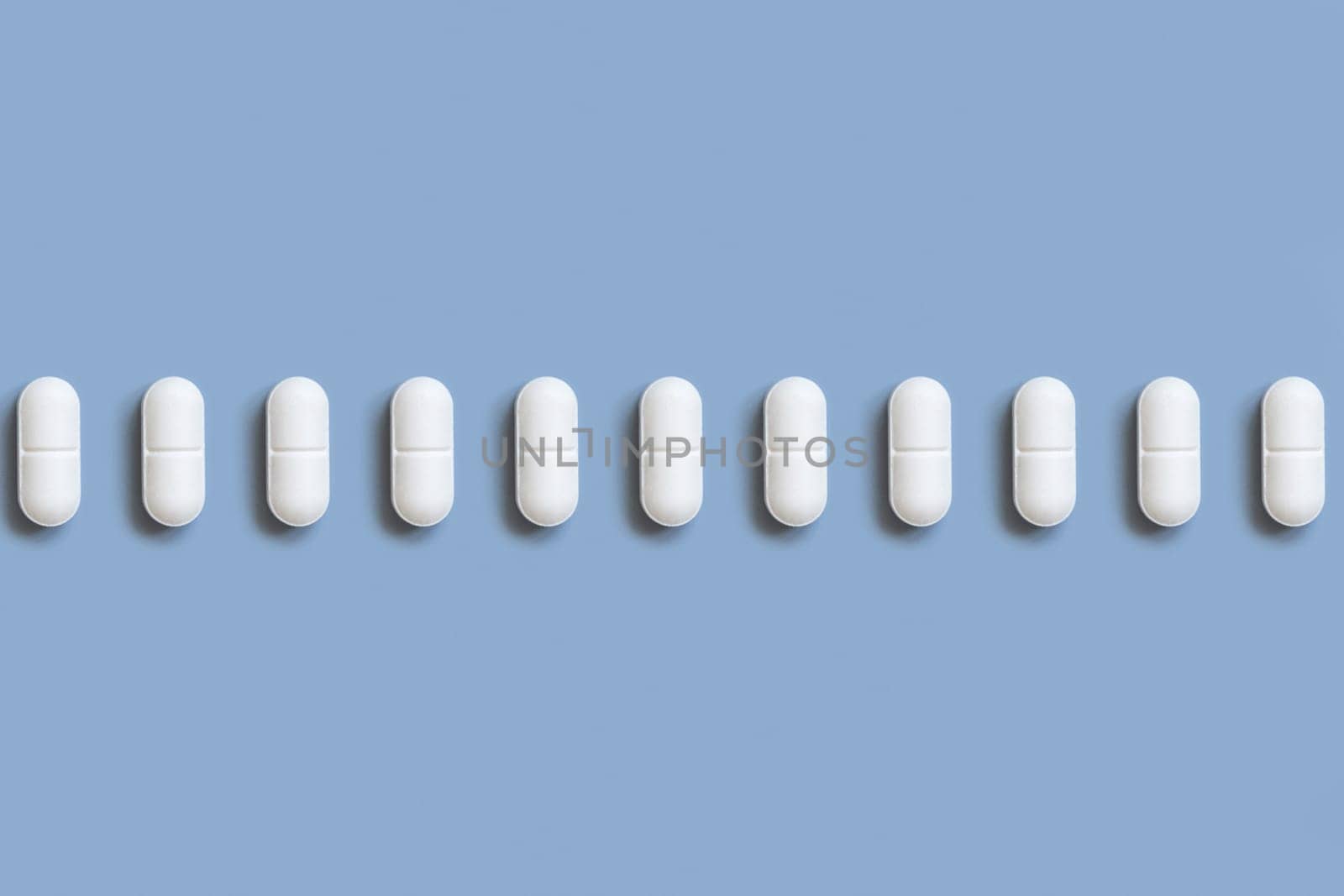 Mix of white medical pills in a line on light blue top view. Preventive medicine and healthcare, dietary supplements and vitamins. Assorted pharmaceutical medicine capsules