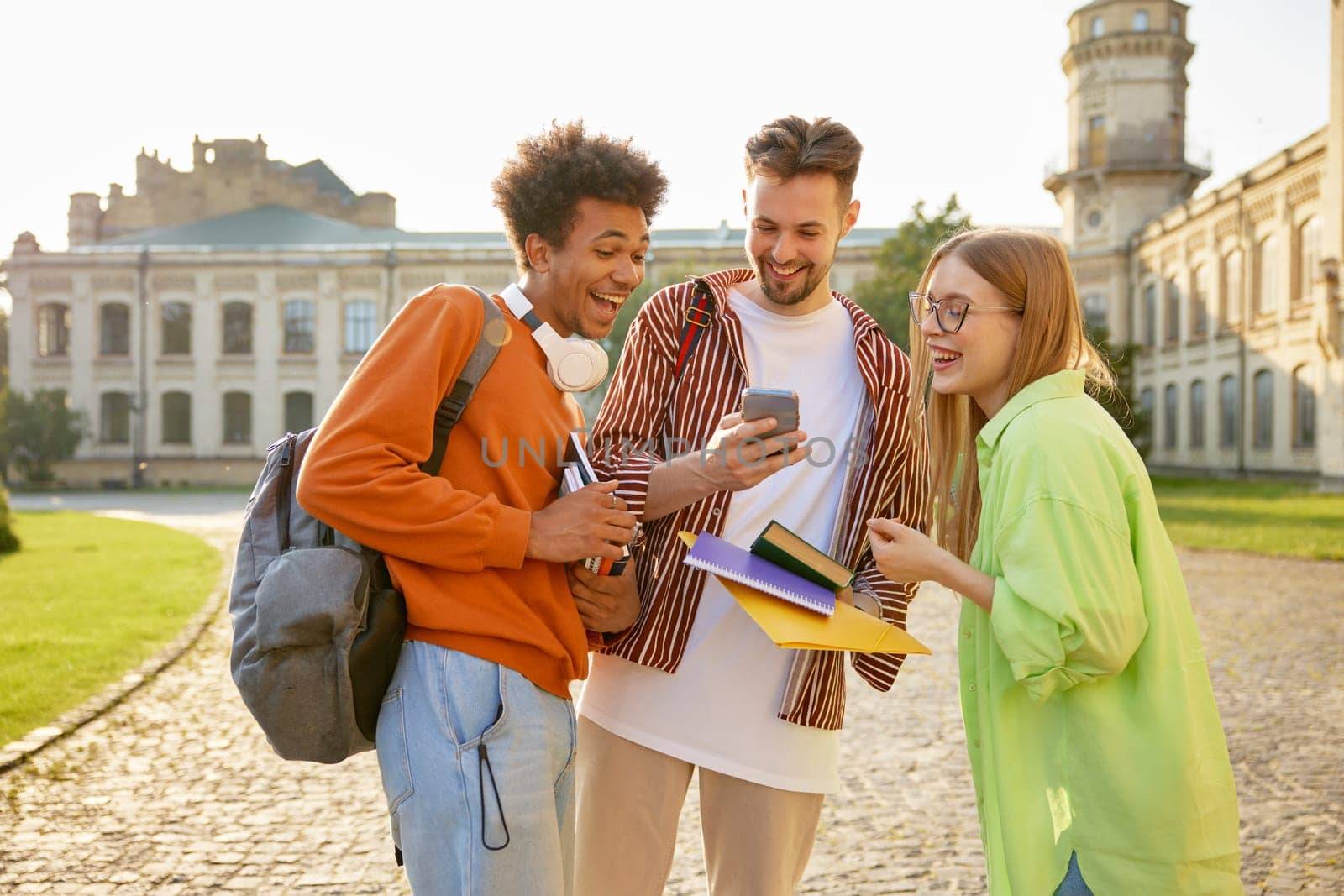 Group of interracial teenager students laughing while watching funny video on mobile phone. Young people friendship and sharing positive vibes