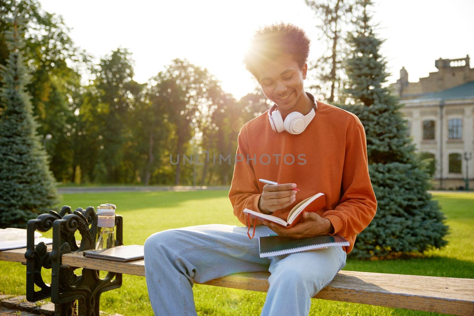 Teenager boy student writing notes in diary book while sitting on bench at university campus. Time management and everyday routine of scholar guy