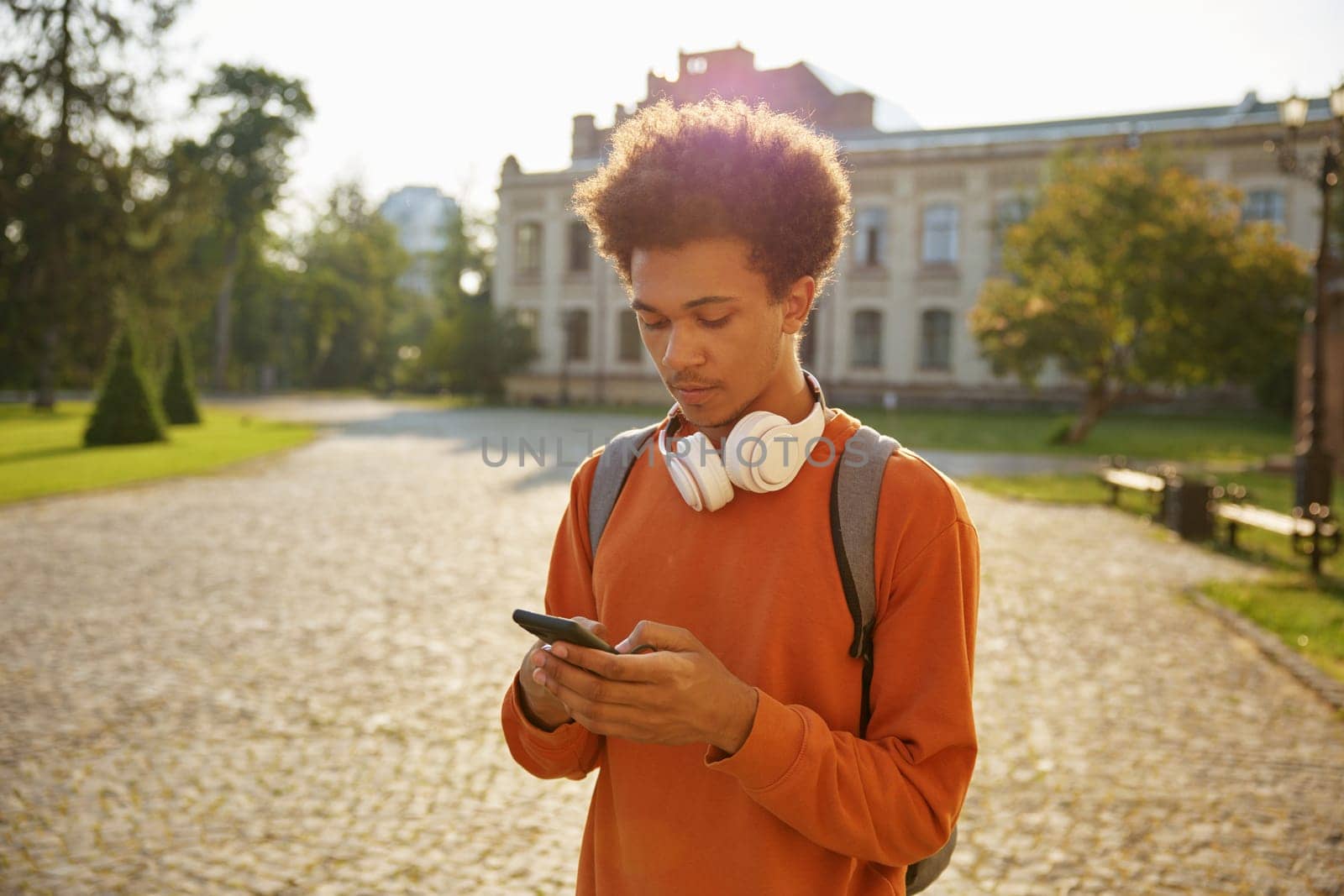 Teenager boy student using mobile phone standing outdoors. Break time at high school, university or college