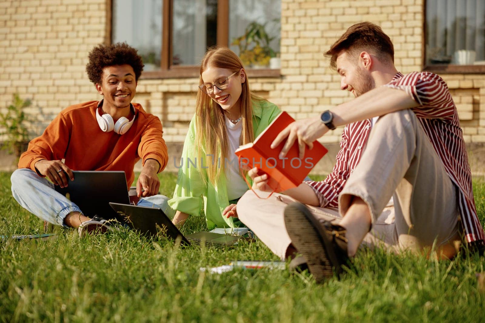 College students studying outdoors, having discussion and preparing for exams at university campus. Happy interracial pupils brainstorming on project together using modern technology