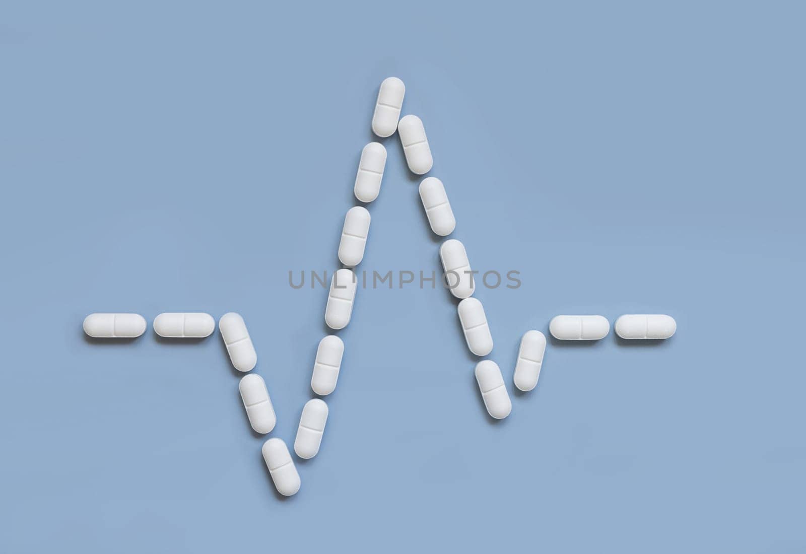 Heart rhythm cardiogram line made of white drug pills and capsules on light blue, top view. Pharmaceutical and cardiology concept, treatment of heart diseases.
