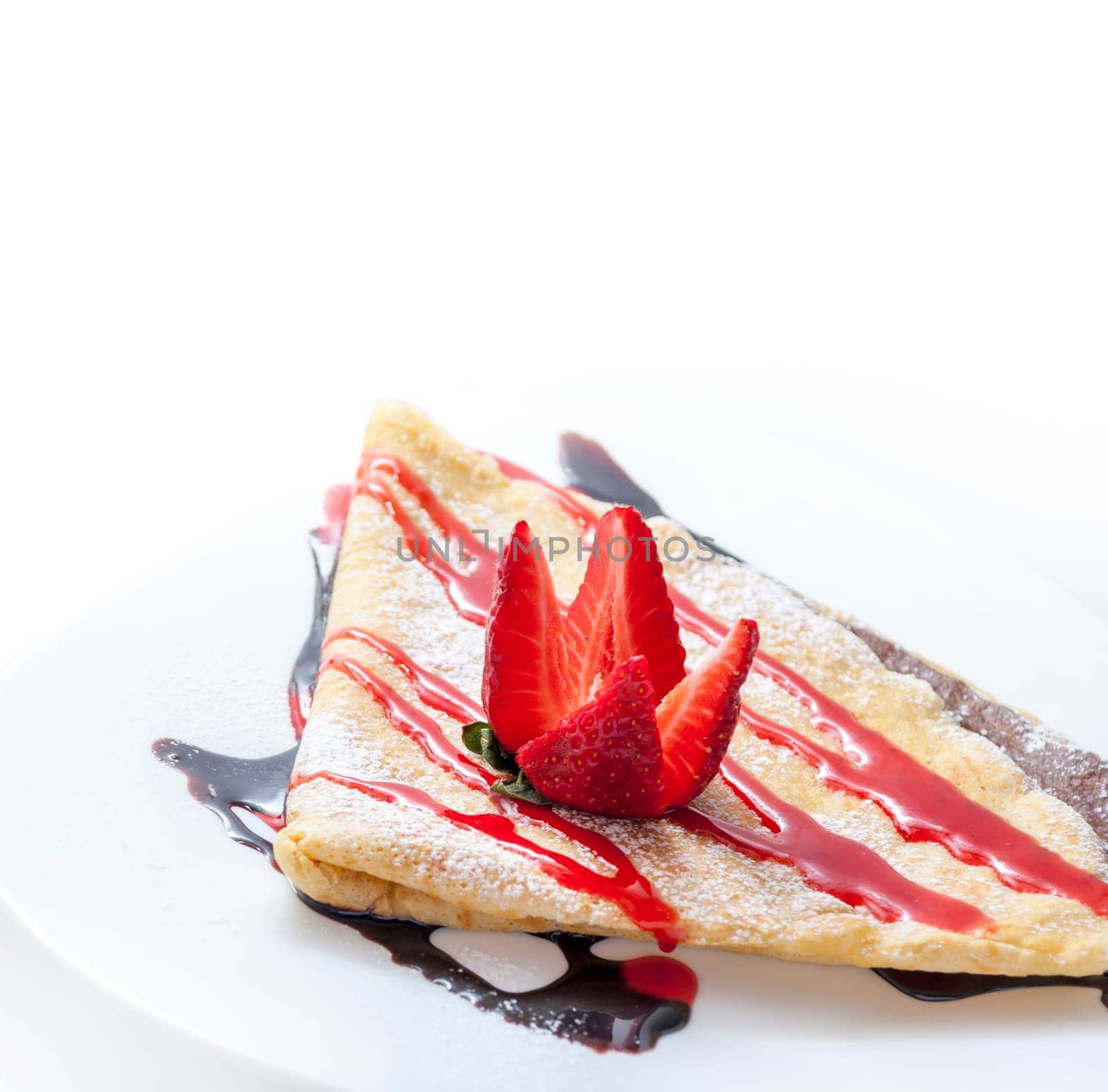 Closeup of sweet french crepes with chocolate and strawberry syrup on restaurant plate. Sweet dessert food with fruit and caramel. Thin pancake breakfast isolated on white background with copyspace.
