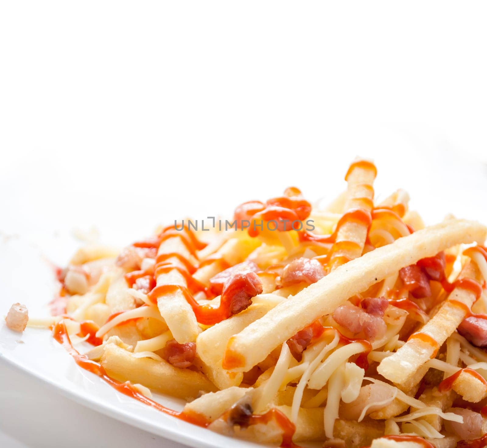 Closeup of french fries served in restaurant plate isolated on white background. Fried potato with ketchup, cheese and bacon. Fast food restaurant menu.