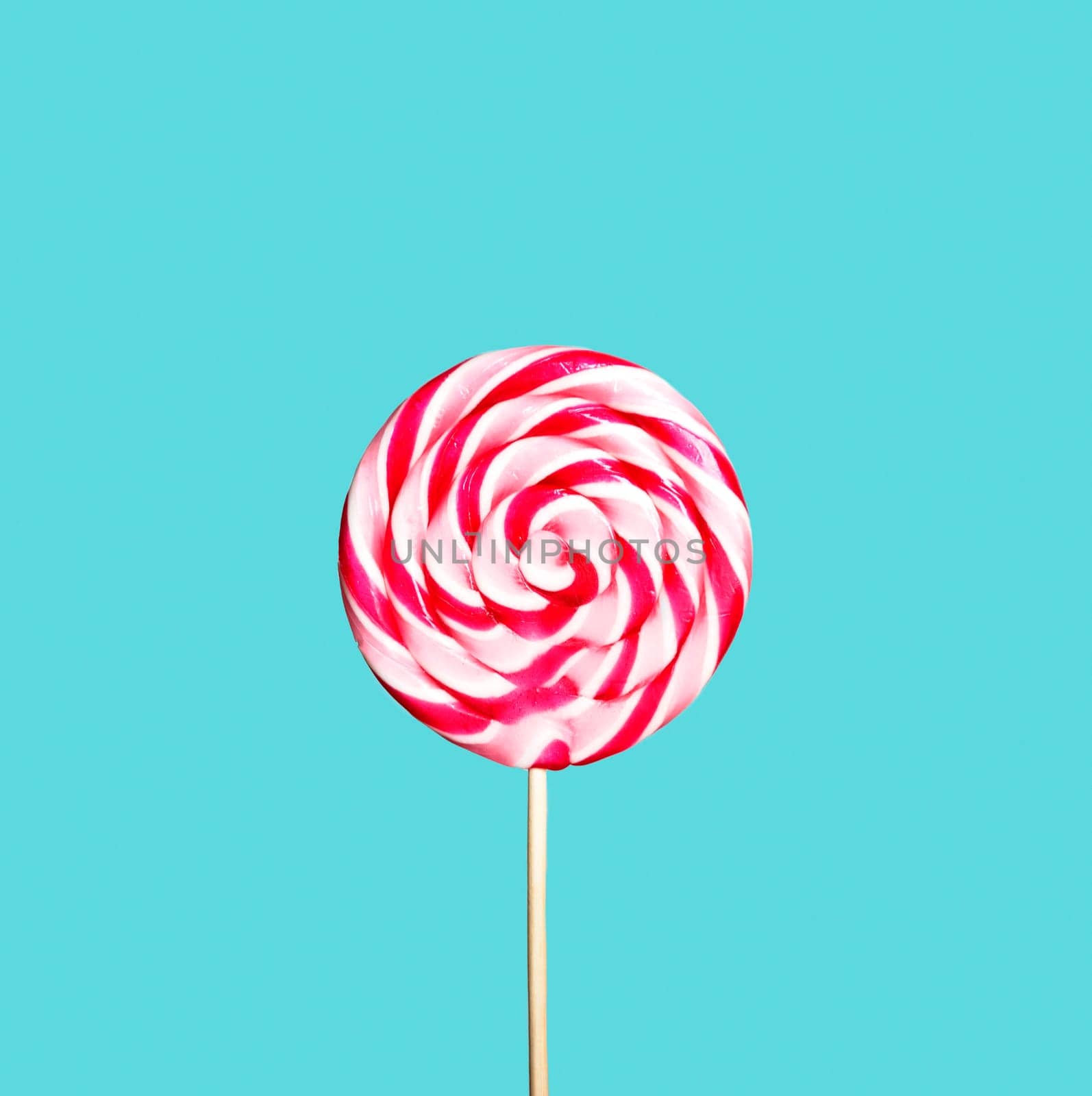 Colorful red and pink lollipop on pastel blue background. Sweet sugar candy swirl in modern fashion style. Minimal flat lay design. Food fun for kids concept.