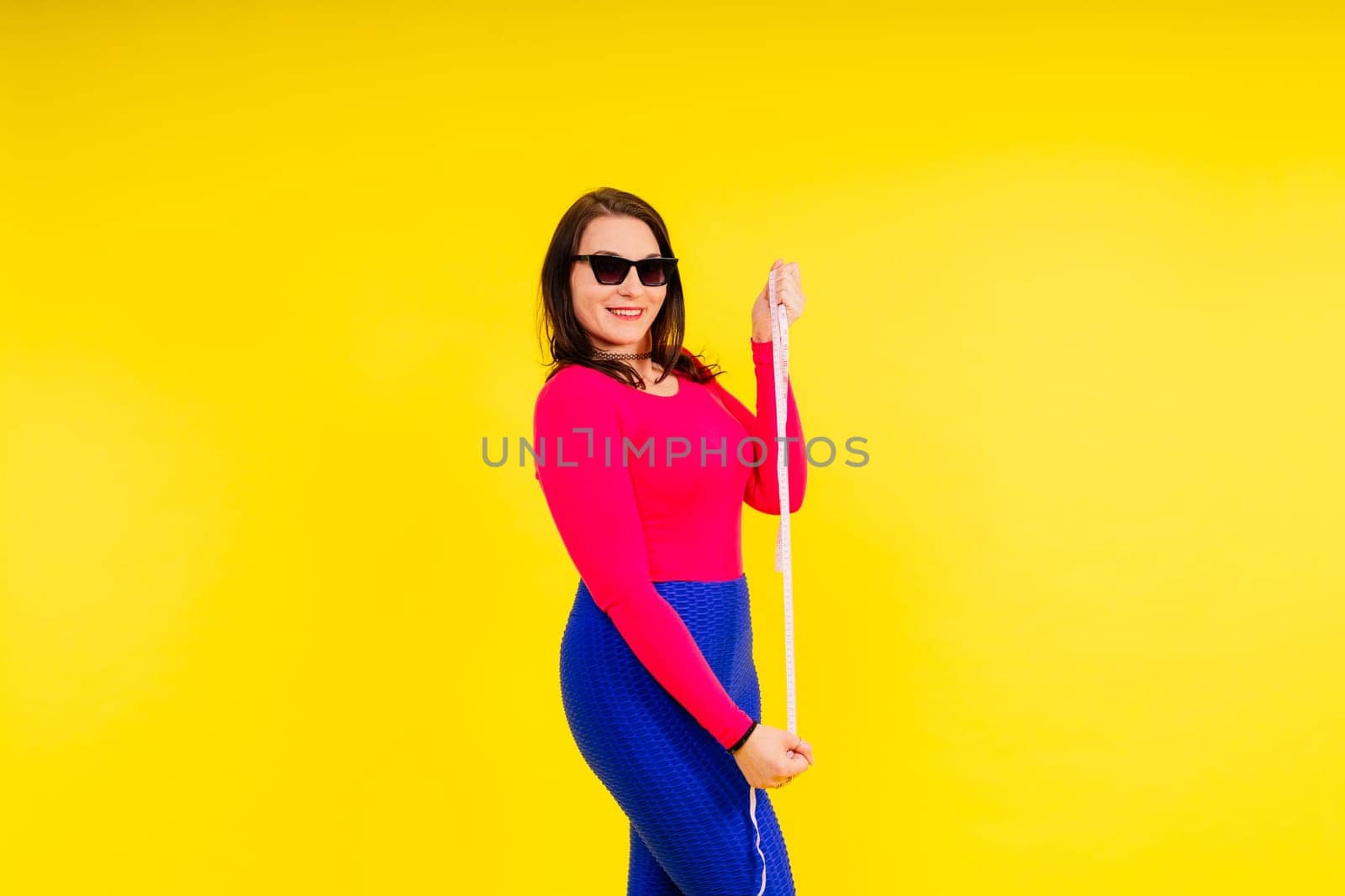 Overweight woman measuring waist before weight loss in a studio shot on yellow background