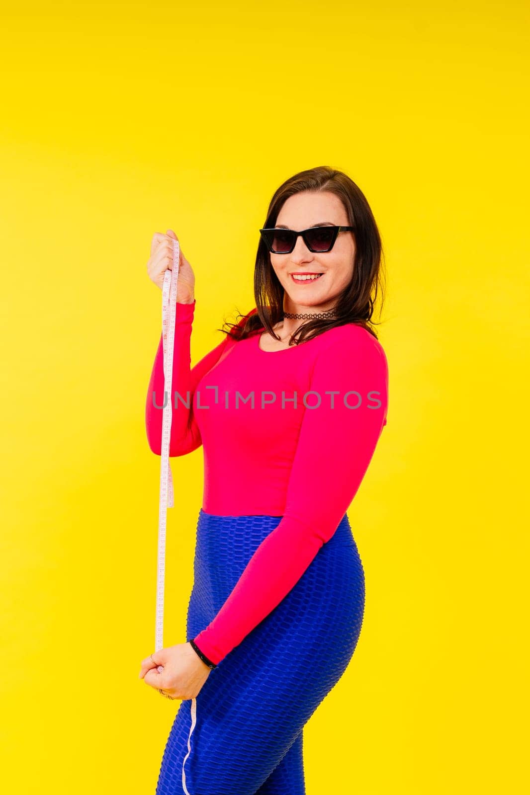 Overweight woman measuring waist before weight loss in a studio shot on yellow background