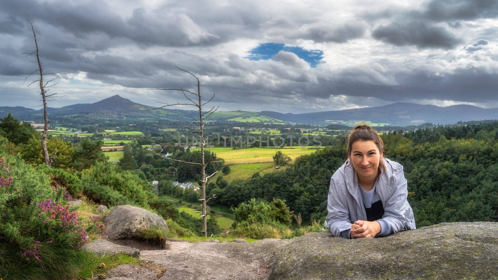 Adult woman leaning over a rock in Lead Mines, with a beautiful view on a valley and forest in background. Hiking in Wicklow Mountains, Ireland