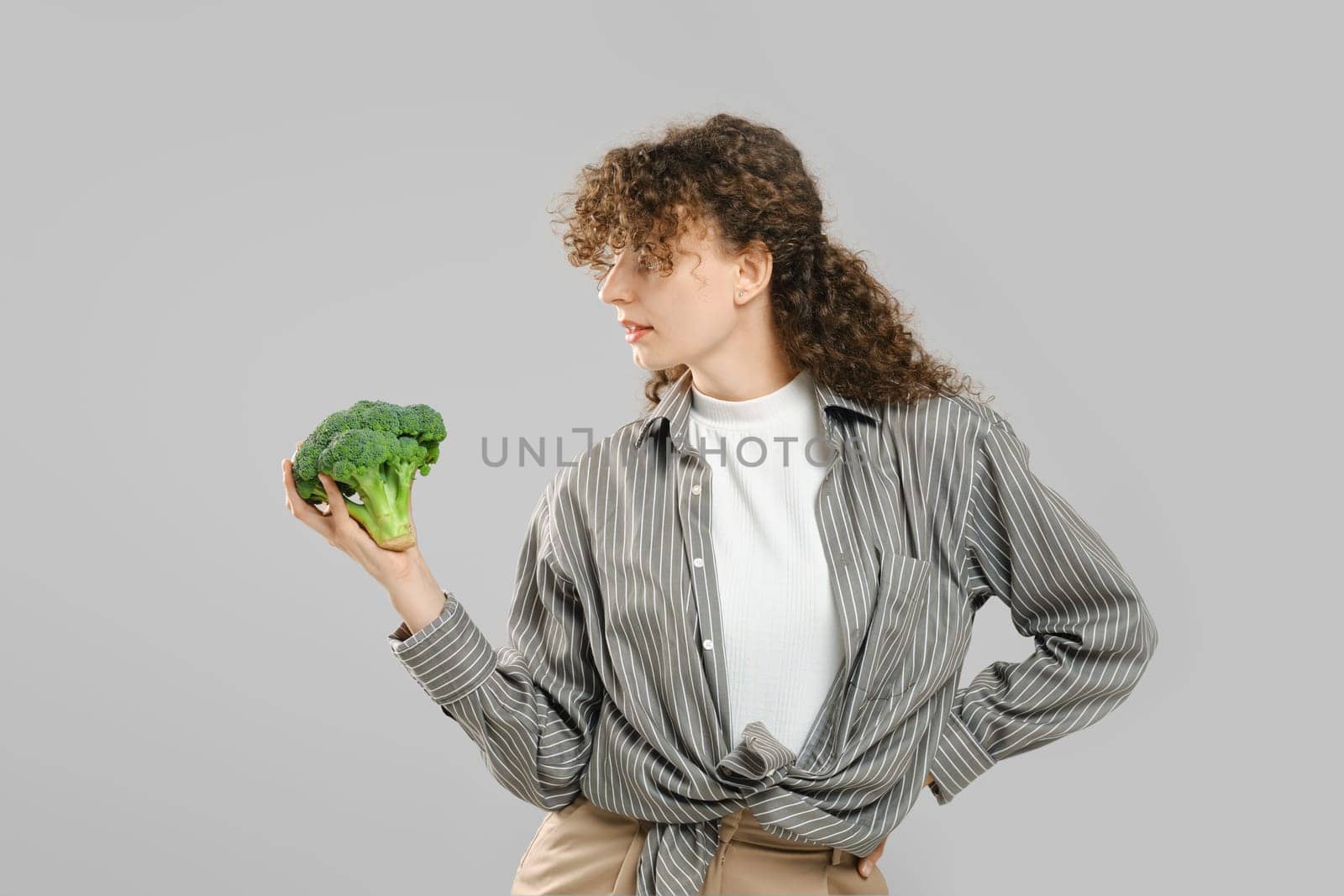 Woman with long curly hair holds broccoli in hand and looking at it