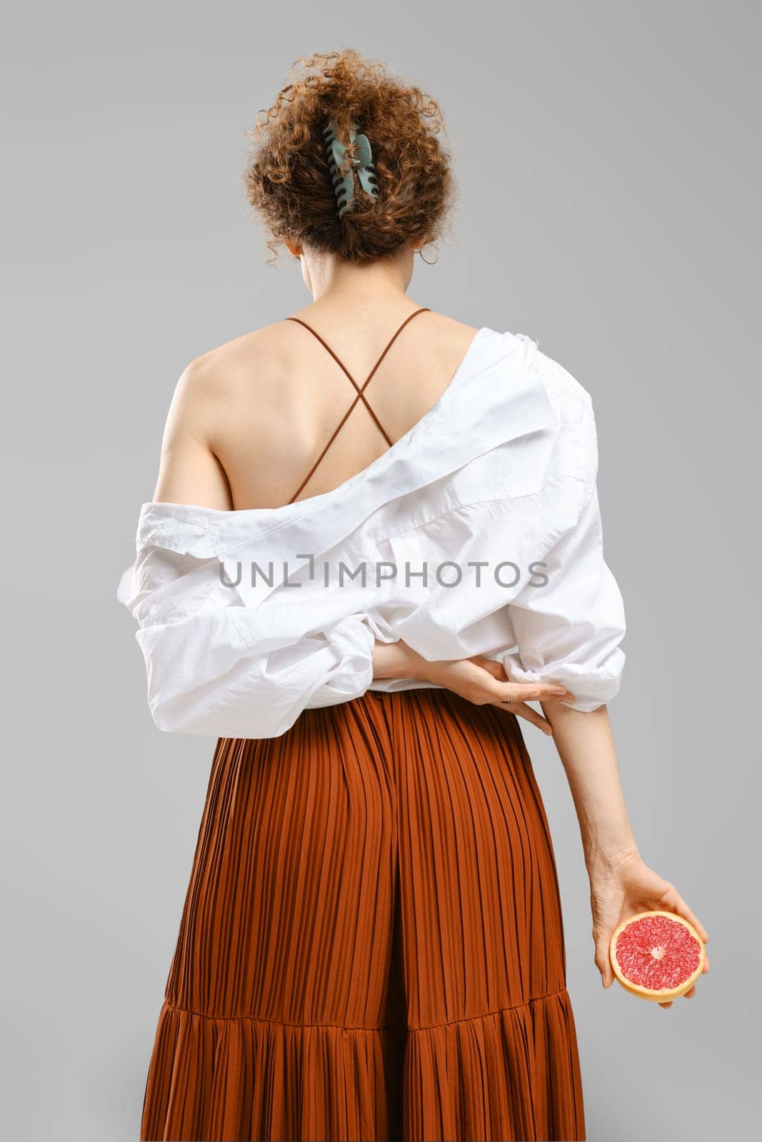 A woman has her back turned and holds half a juicy grapefruit in one hand