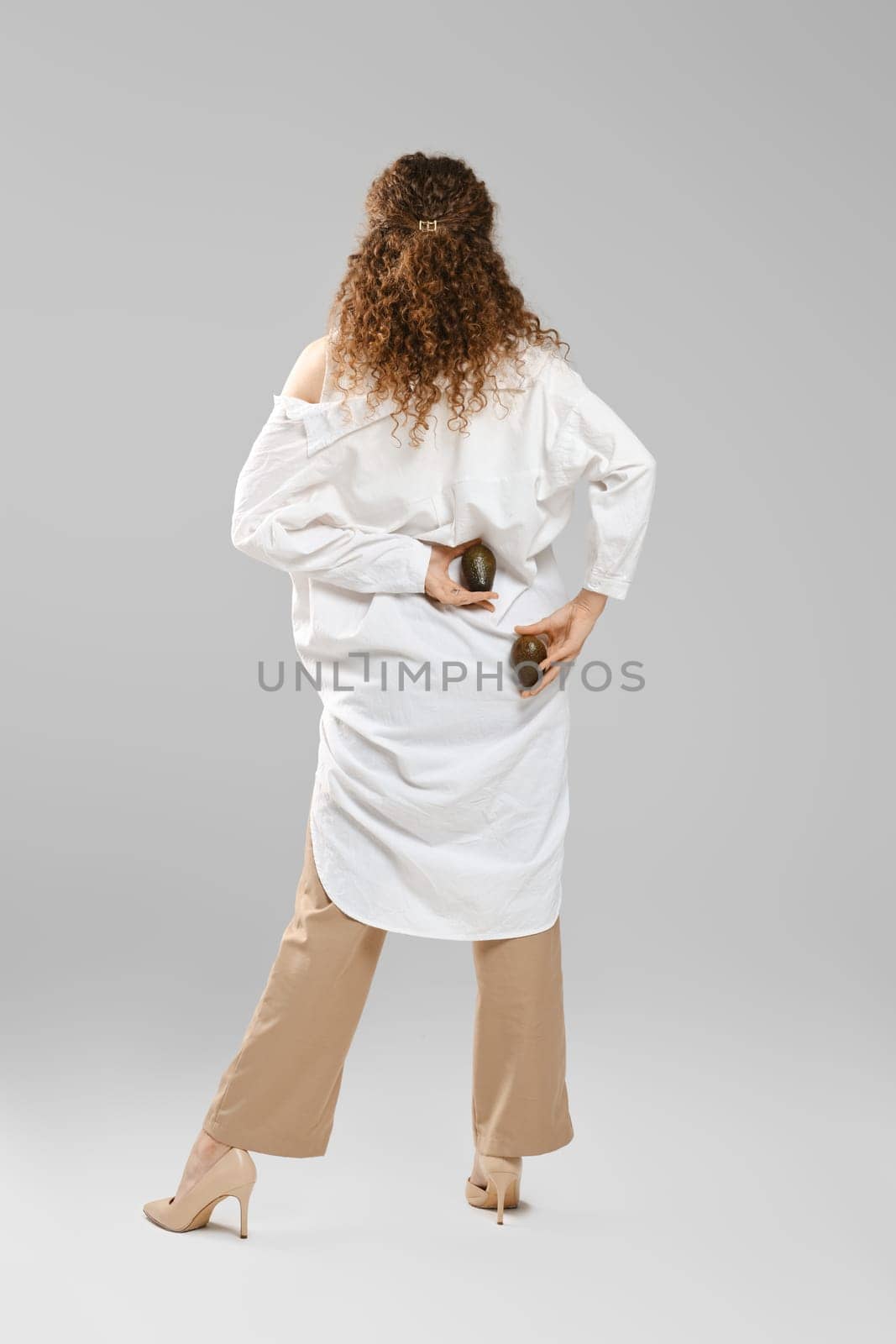 Back view of woman holding two whole avocado behind her back