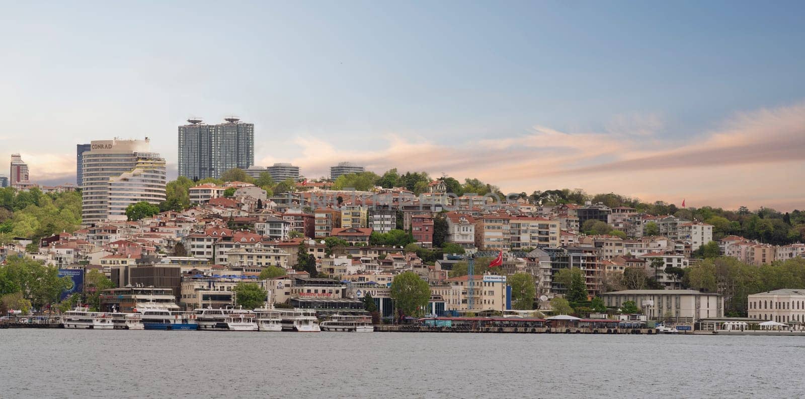 European side of the Bosphorus Strait, Istanbul, Turkey, with a ferry boat floating on the water, and city skyline in the background. The sky is clear, and the water is calm