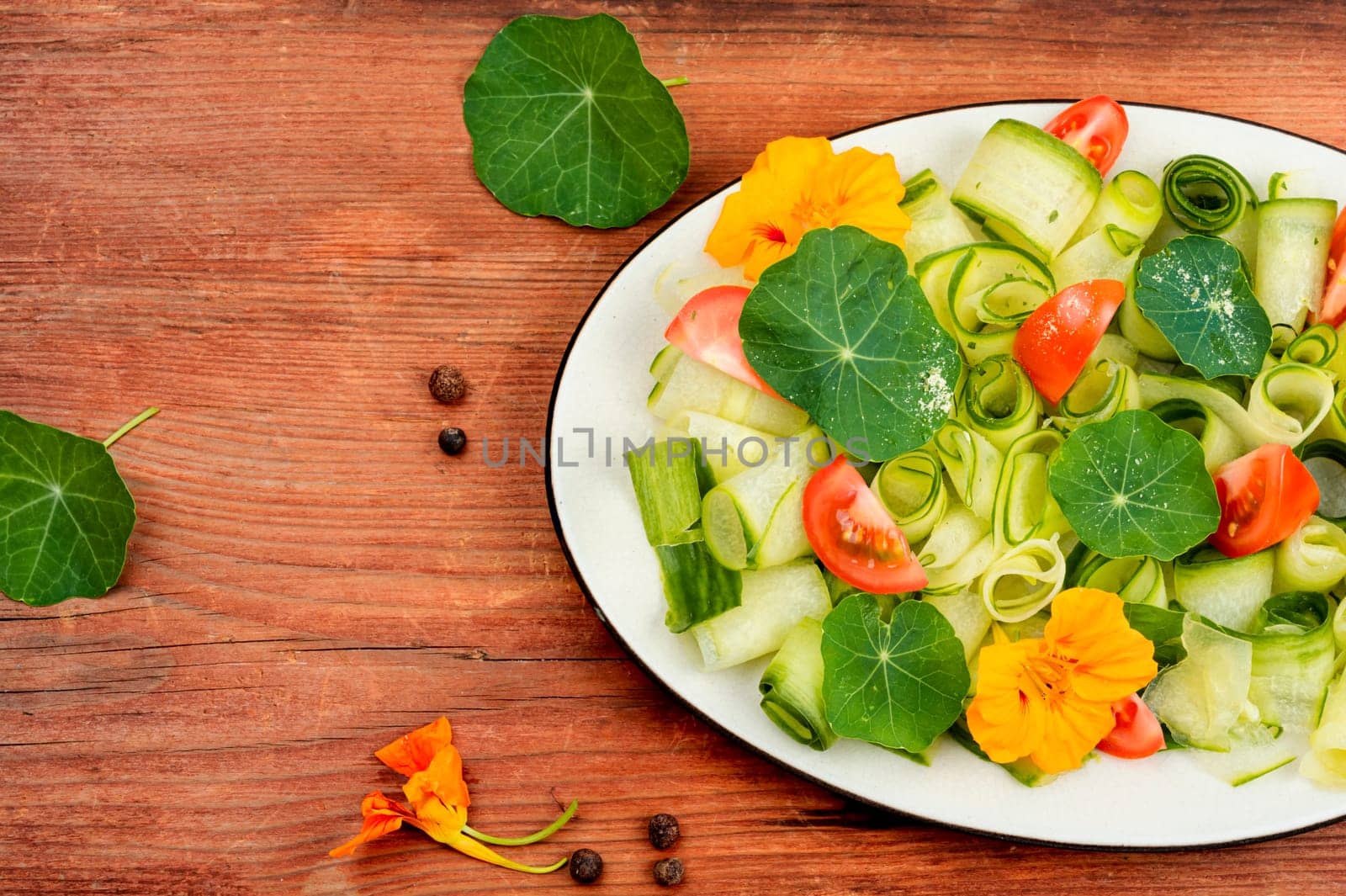 Rural salad with vegetables, nasturtium and dressing on wooden table.