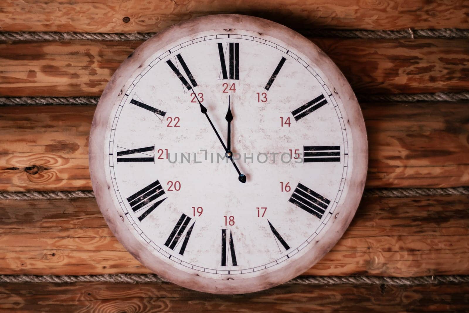 Round vintage clock showing five minutes to noon, midnight hangs on wooden wall. Decorative elements. Countdown. Design. Cozy house . Retro style. Sense of time. Space for text.