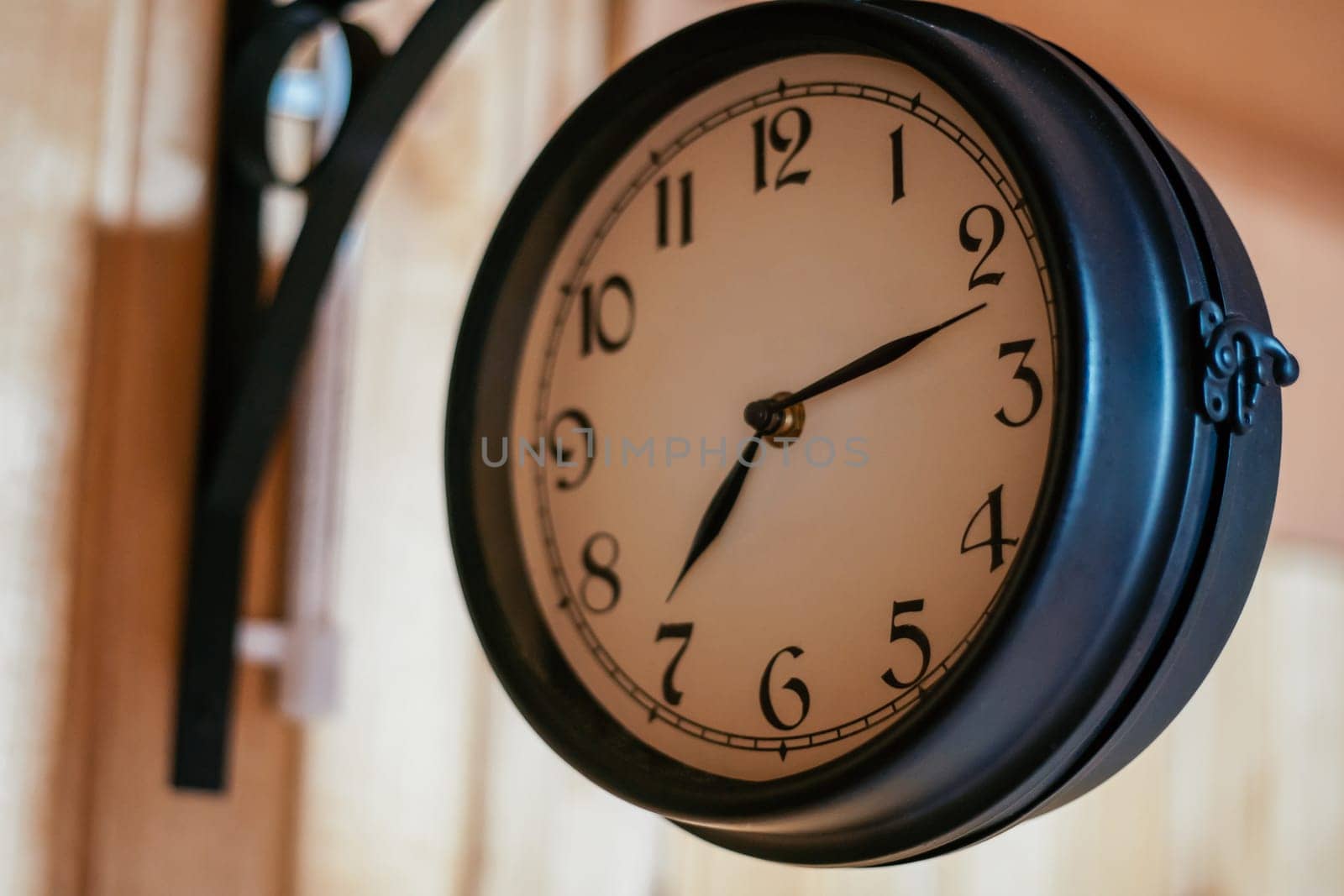 Decorative elements. Round vintage clock in black metal hanging on corner mount on wooden wall. Countdown. Design. Cozy house . Retro style. Sense of time. Round clock signboard.