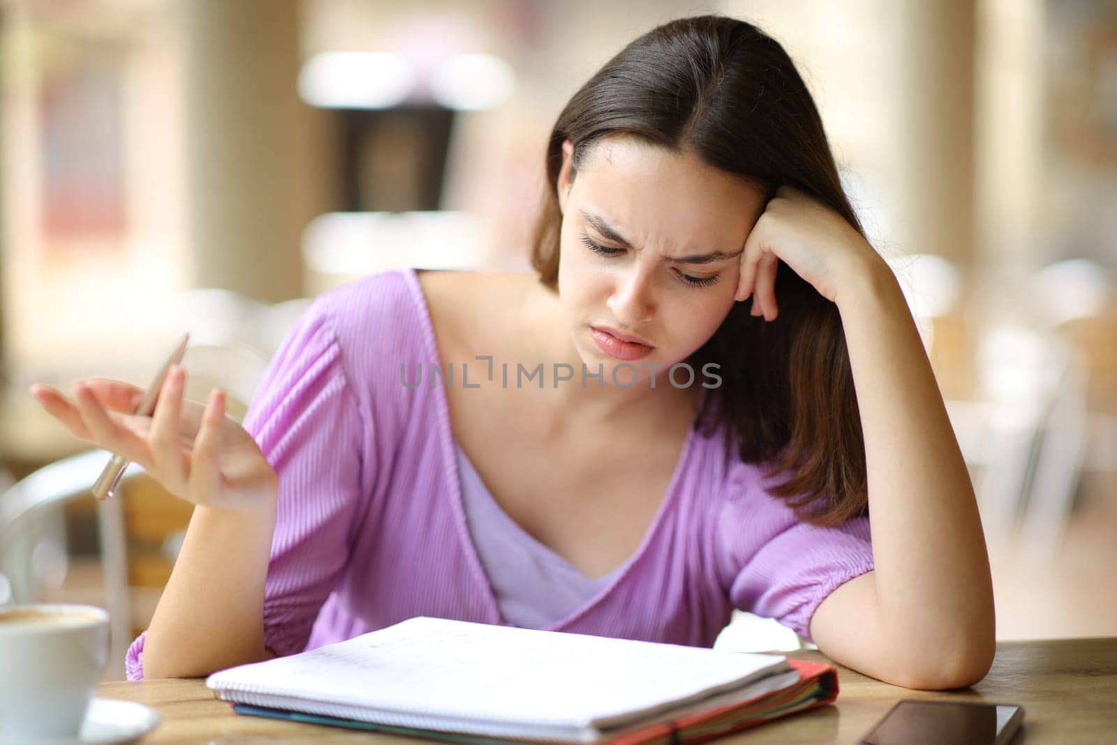 Confused student checking lesson on notebook in a bar terrace