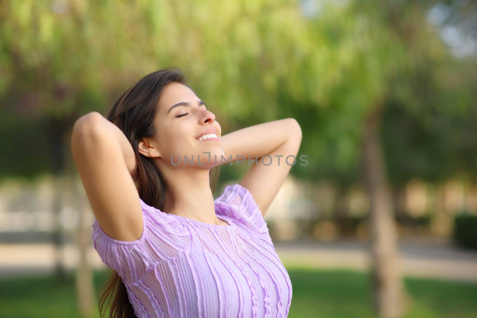 Happy woman relaxing with hands on head in a park alone