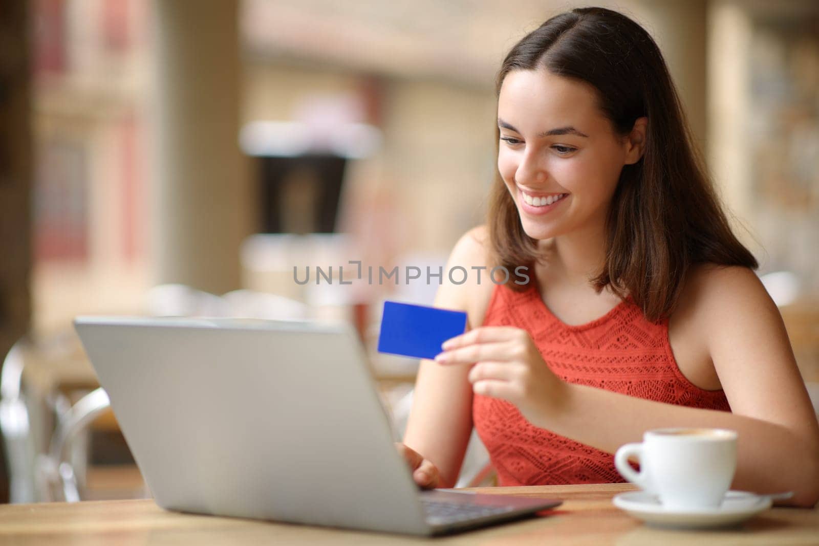 Happy woman with laptop and credit card buying online in a bar terrace