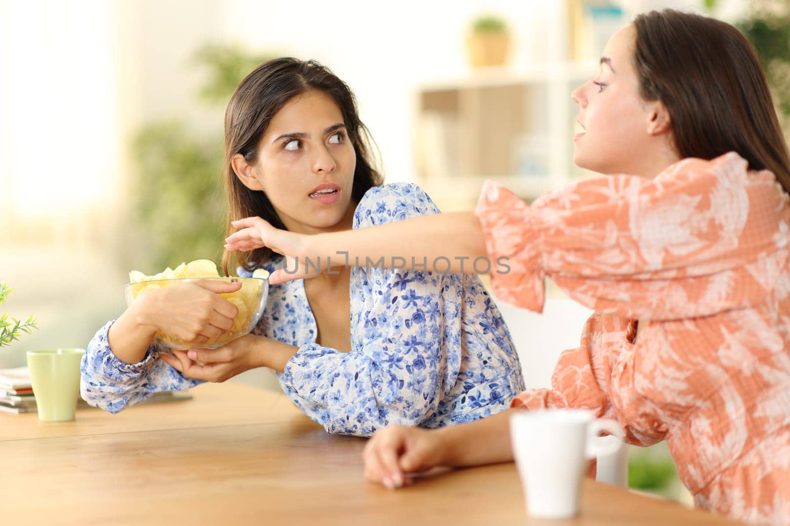 Woman trying to eat potatto chips and selfish friend avoiding at home