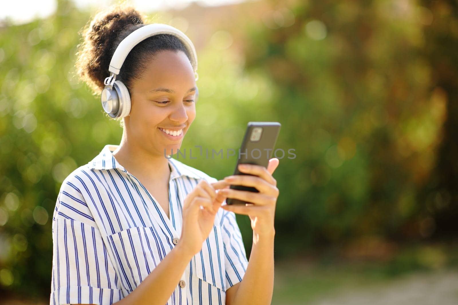 Happy black woman listening audio with headphone and cell phone in a park