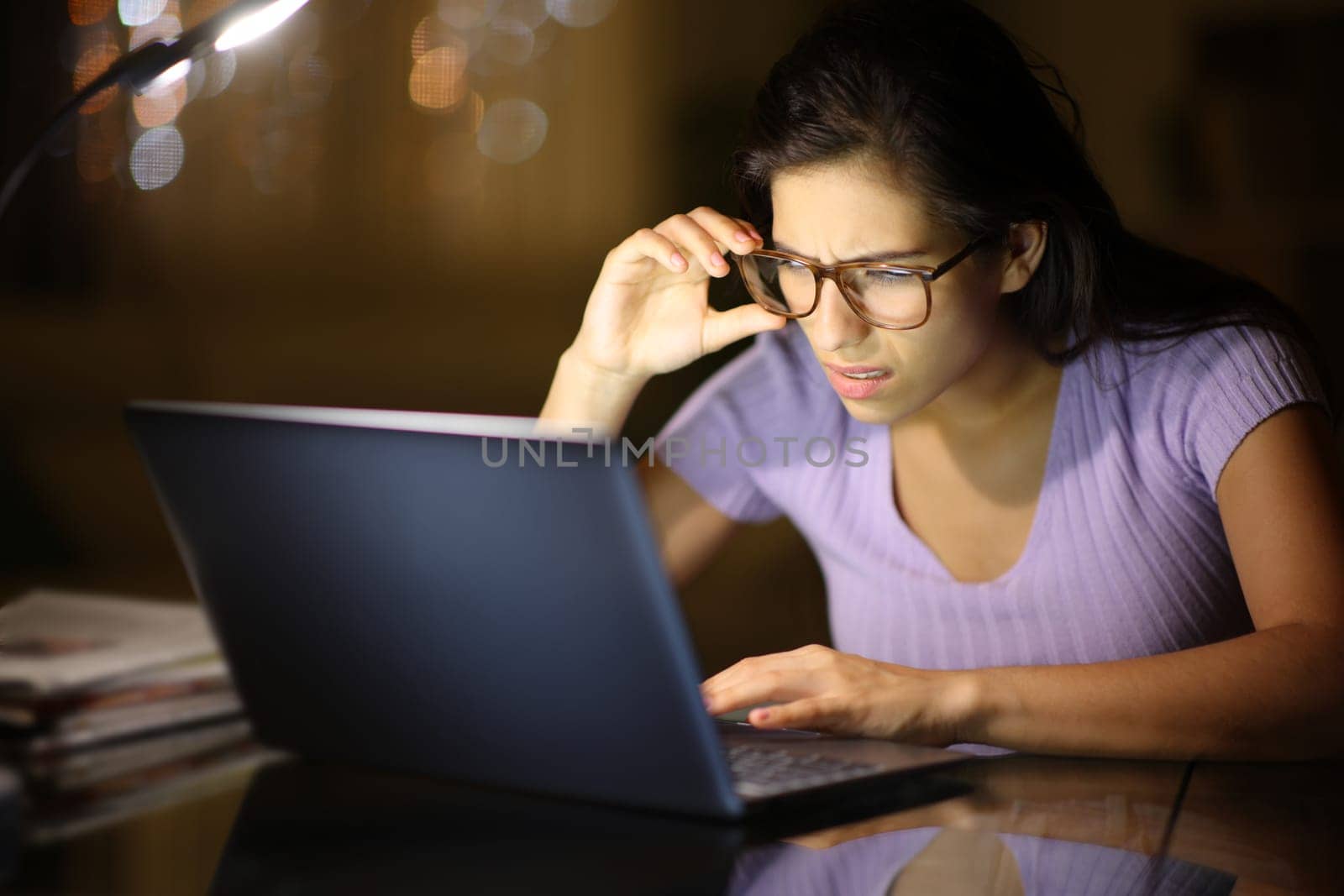 Woman using eyeglasses forcing sight with laptop in the night at home