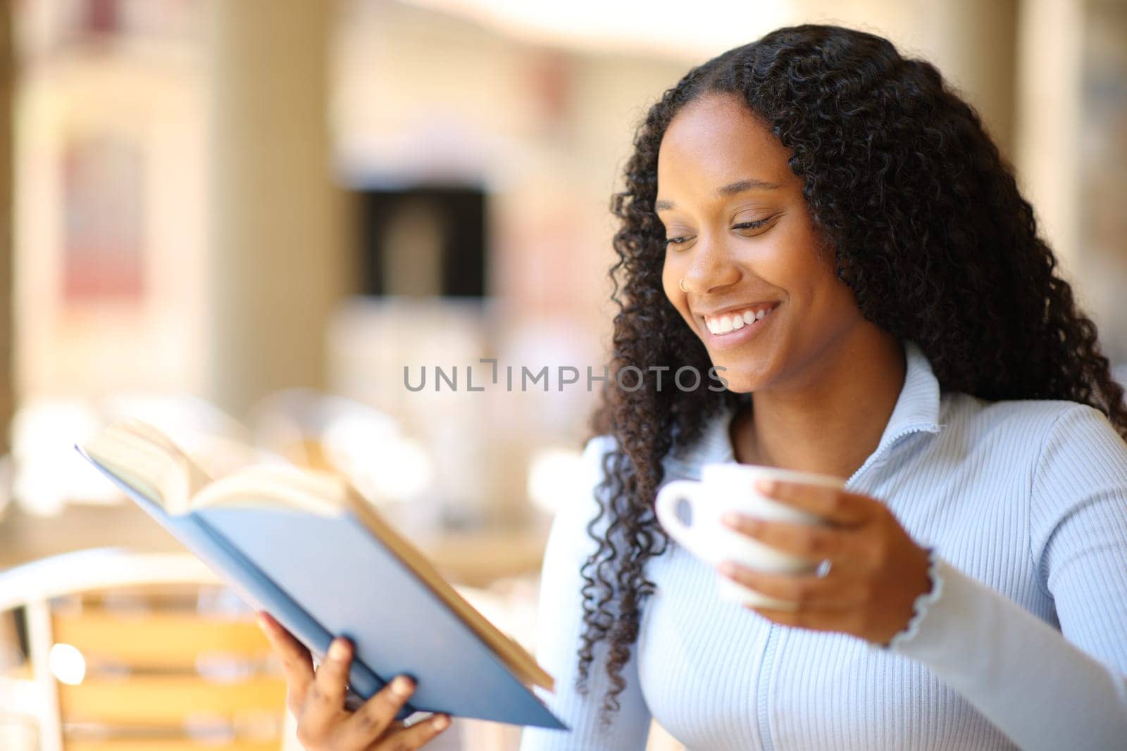 Happy black woman reading a paper book sitting in a coffee shop terrace