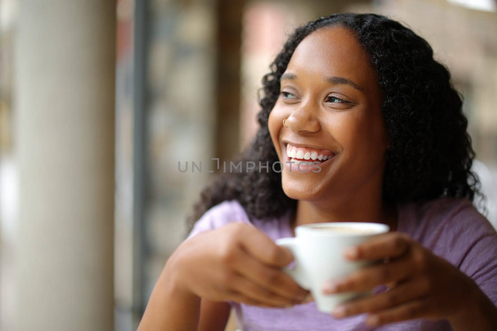 Happy black woman drinking coffee and laughing looking at side in a restaurant terrace