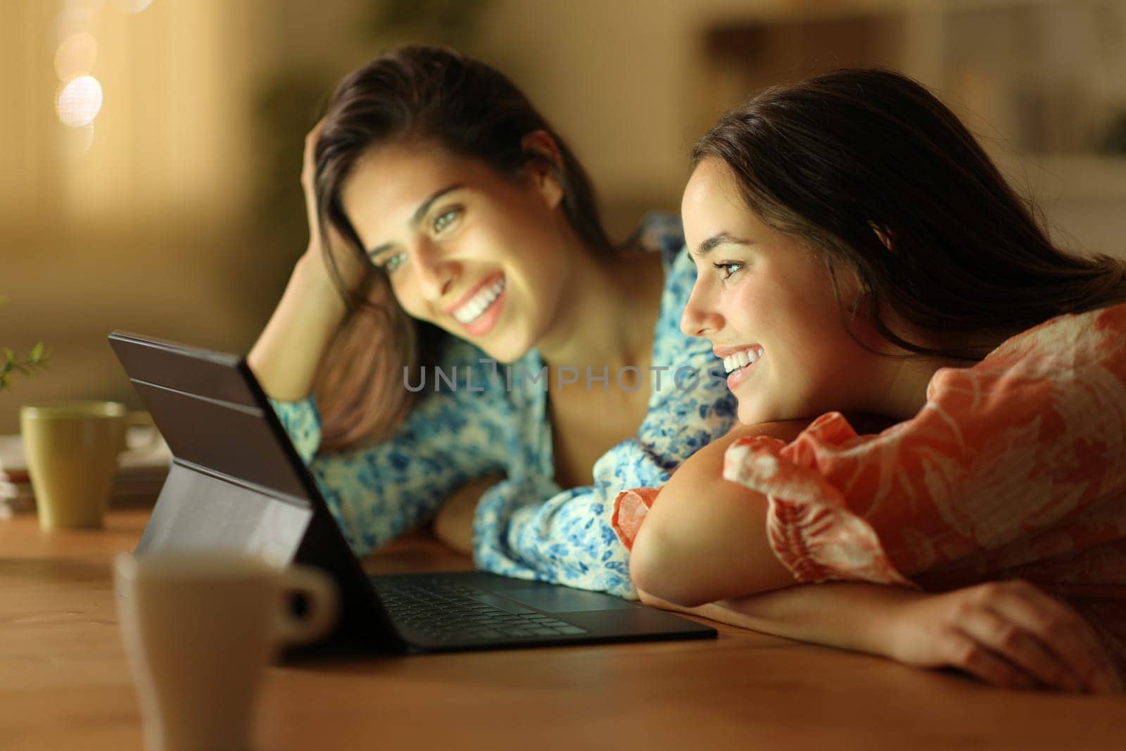 Two happy women watching media on tablet in the night at home
