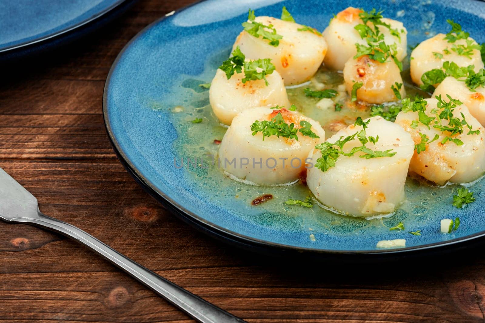 Roasted scallops with green, grilled sea scallops in creamy sauce. Wooden background.