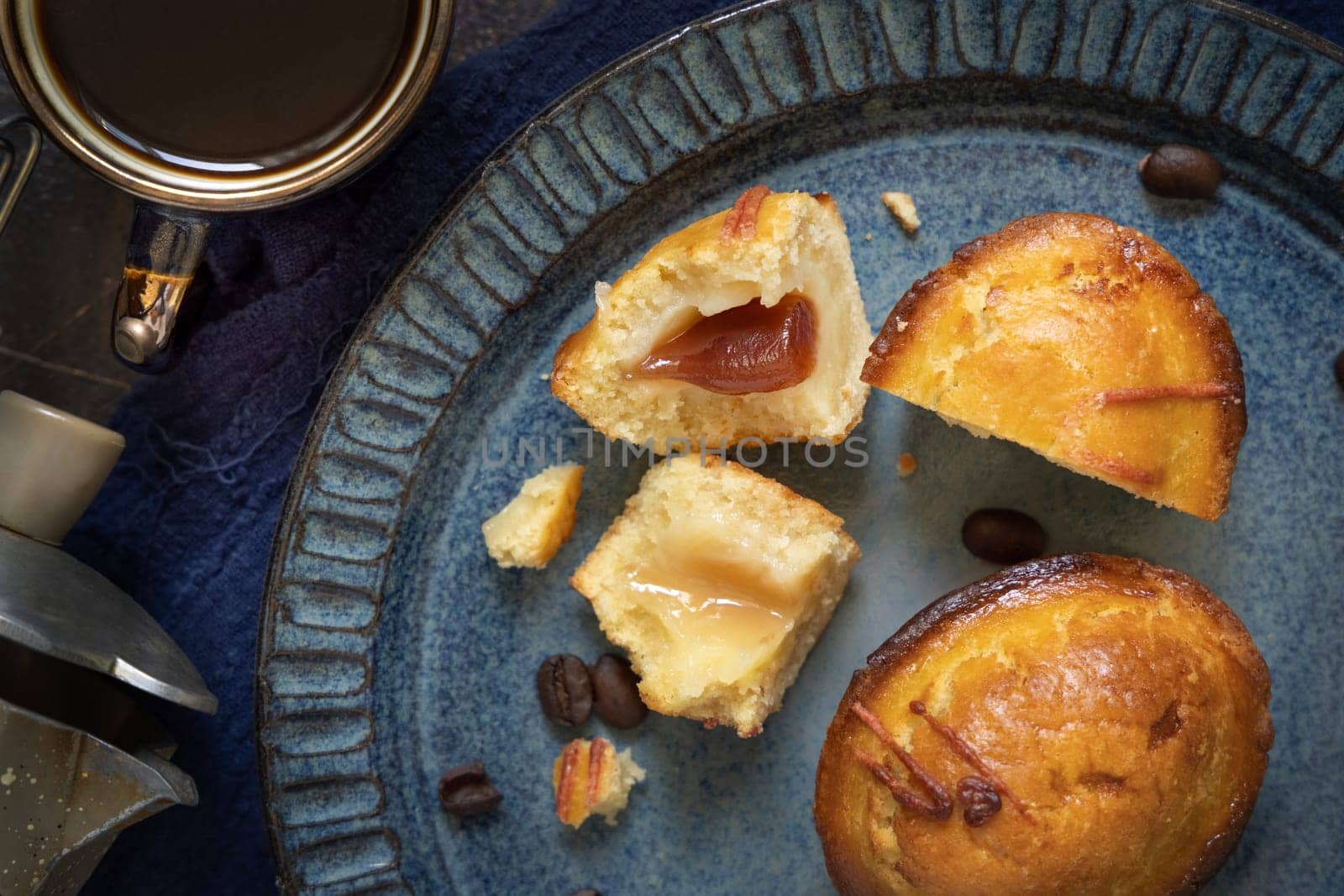 Pasticciotto leccese pastry filled with egg custard cream and sour cherry jam. Pieces of pasticiotto on a dark blue plate, typical apulian breakfast, top view. Table decorated with coffee beans