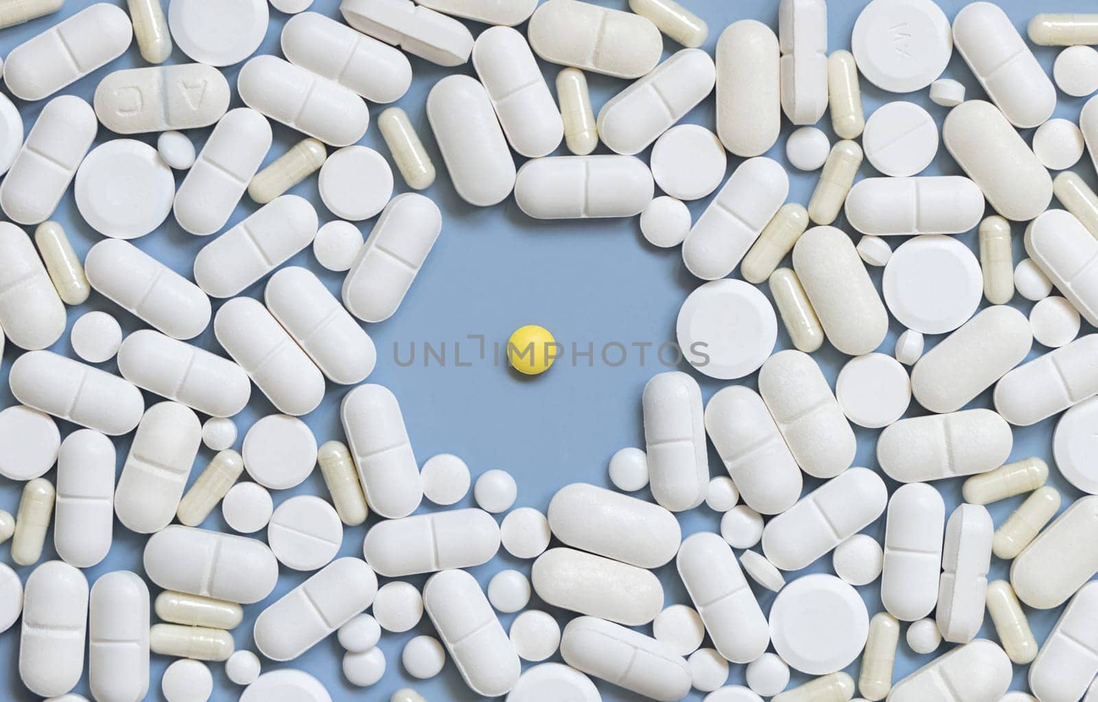 Mix of white medical capsules and pills with one yellow pill in the middle on light blue top view. Medicinal treatment. Taking dietary supplements and vitamins. Assorted pharmaceutical products
