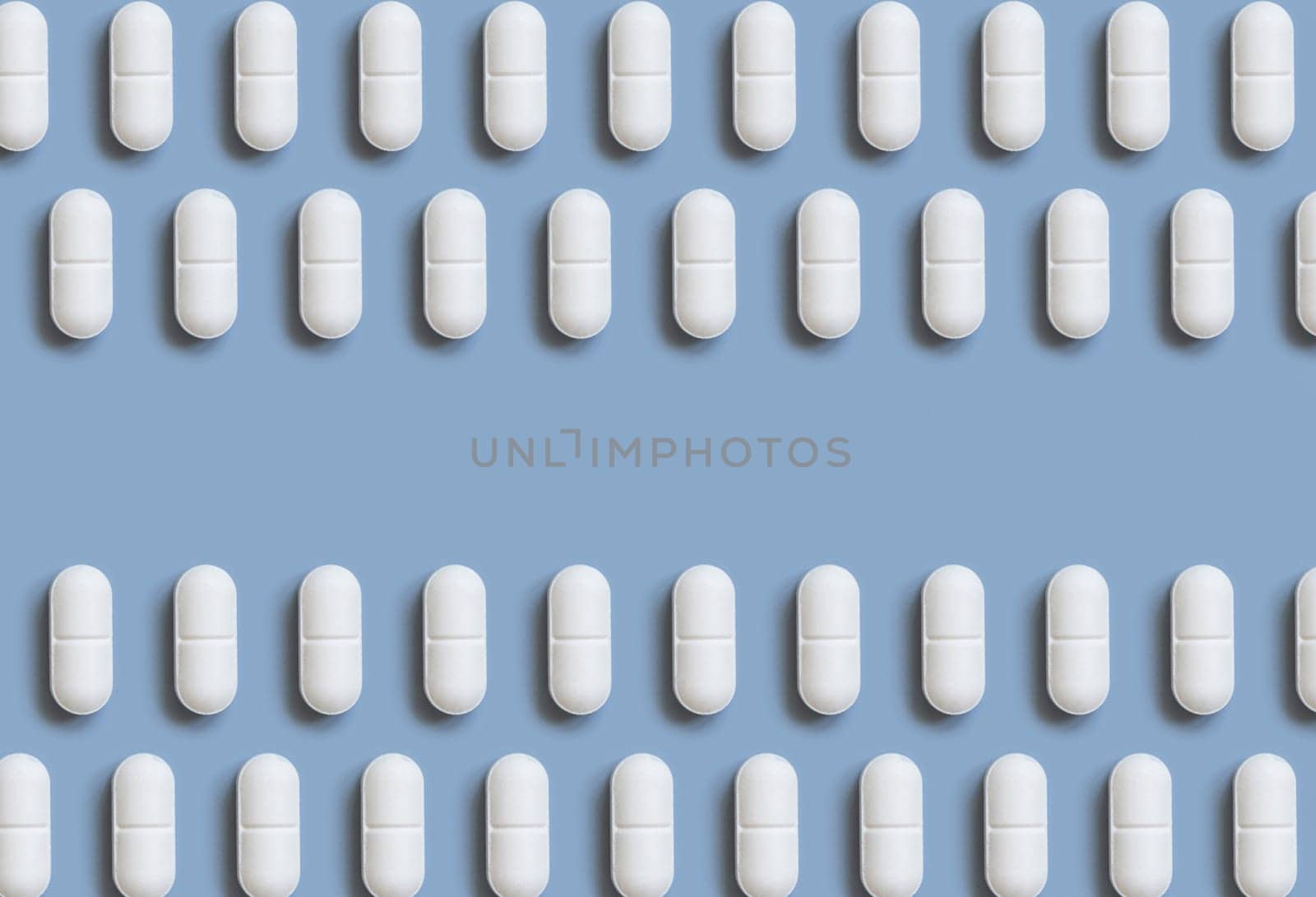 White pills on light blue top view, creative pattern. Curative medicine and healthcare, taking dietary supplements and vitamins. Pharmaceutical pills