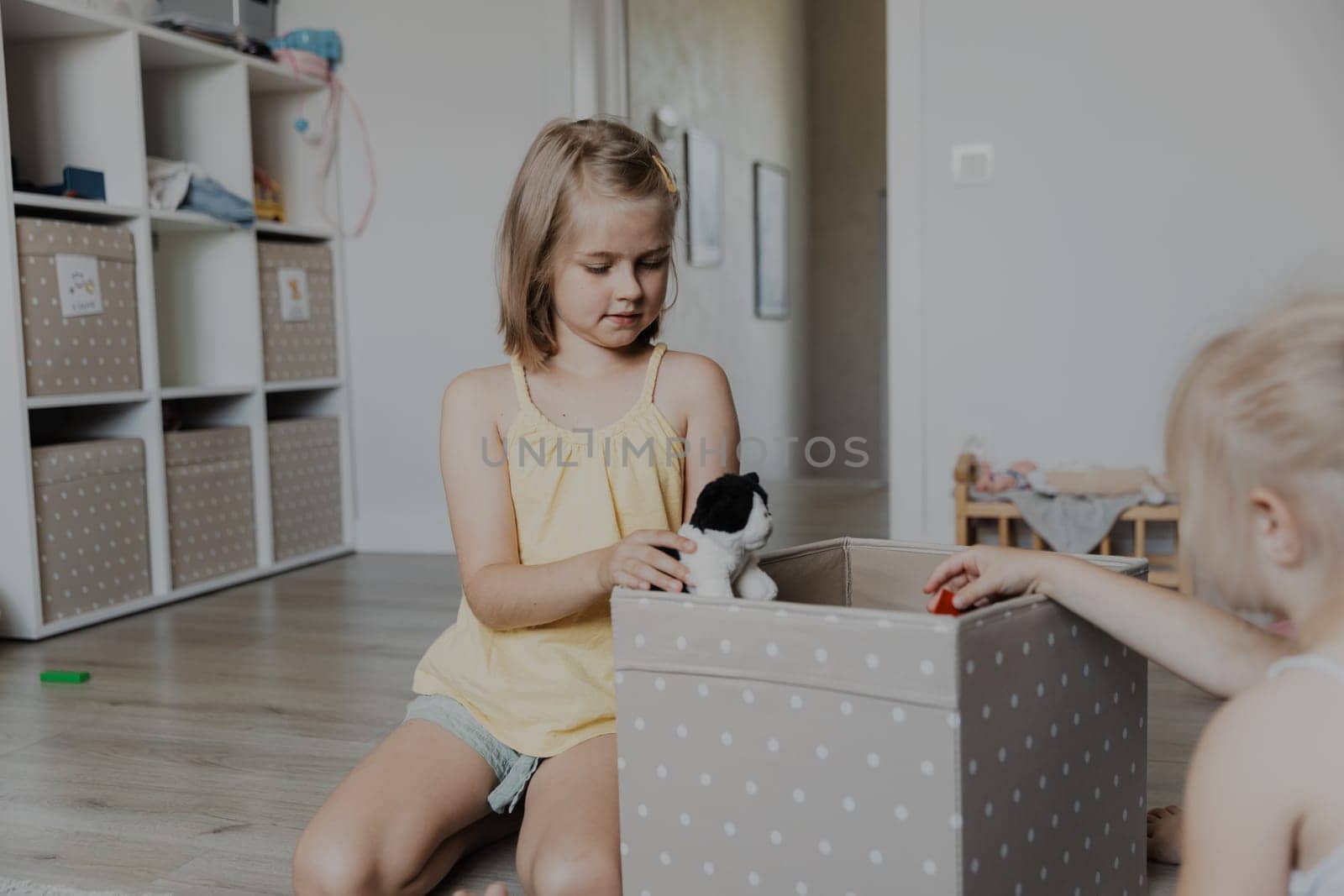 Children cleaning toys from floor after playing, collect them to textile box. Kids sitting on carpet at white home bedroom, kindergarten playroom or playground center. Educational eco-friendly games