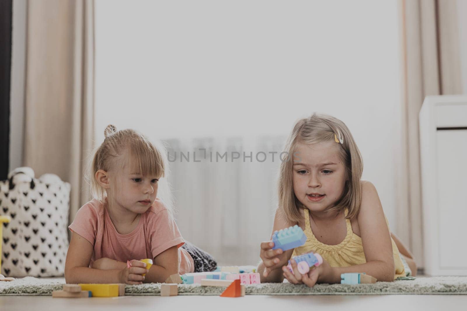 Children playing with colorful toys. Kids sitting on carpet at home bedroom or kindergarten, nursery. Educational eco-friendly game for child. Concentrated creative preschool age sweet sisters