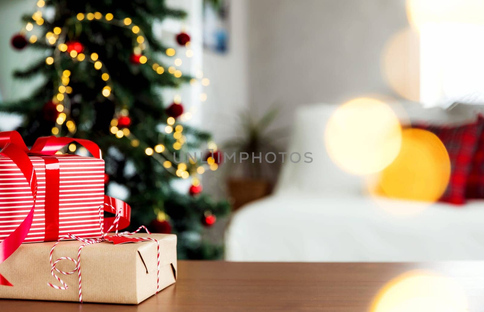 Christmas, New Year background with copy space. Empty wooden tabletop surface, defocused decorated Christmas fir tree composition, bokeh sparkle lights effect, red gift boxes. Product montage mockup