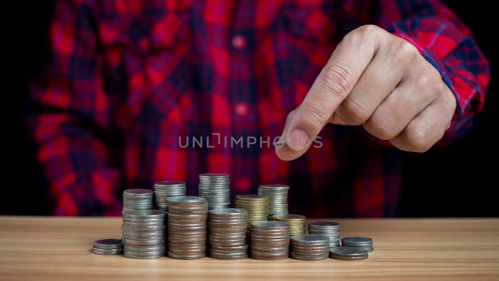 Human puts money on pile of coins. Ideas for investing and growing a business, maximizing profits from business, ideas for setting savings goals and setting goals for fixed deposits with banks.