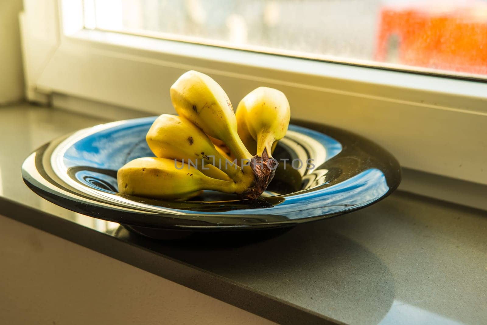 ripe bananas in a black fruit bowl on a window sills