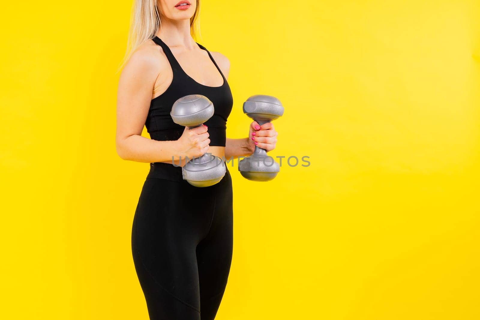 Sporty woman does exercises with dumbbells on dark, yellow, red background.