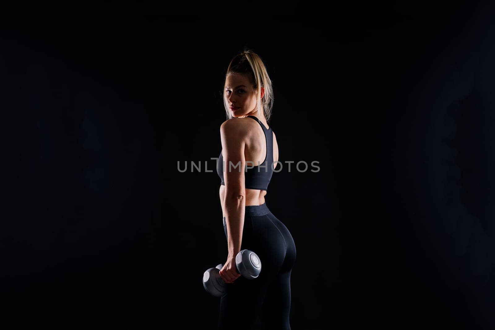 Sporty woman does exercises with dumbbells on dark, yellow, red background.