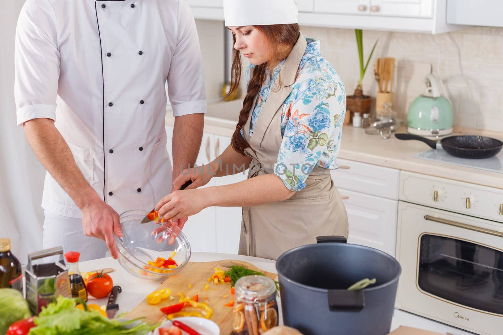 Cook in uniform and his apprentice cooking vegetarian meal