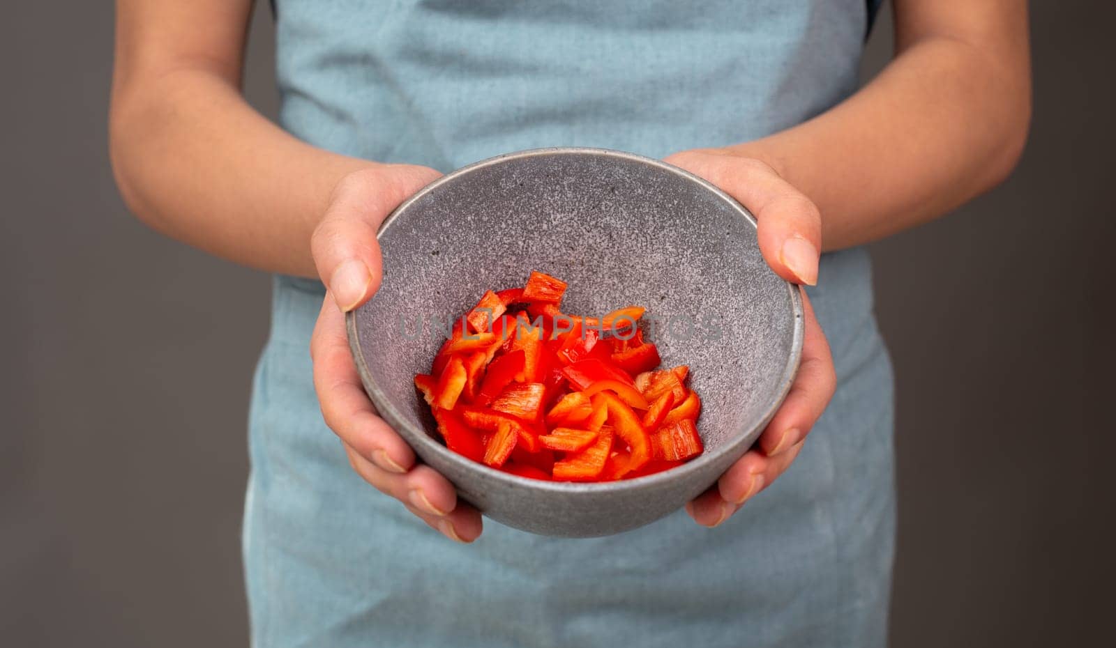 Red sliced pepper pieces in a bowl, prepare healthy food with paprika vegetables, holding fresh organic nutrition in the hands