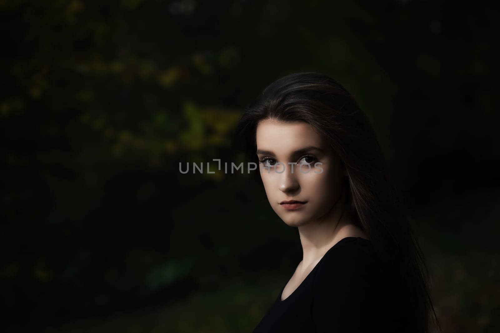 Portrait of cool long haired girl posing outdoors on dark background.  Horizontally.