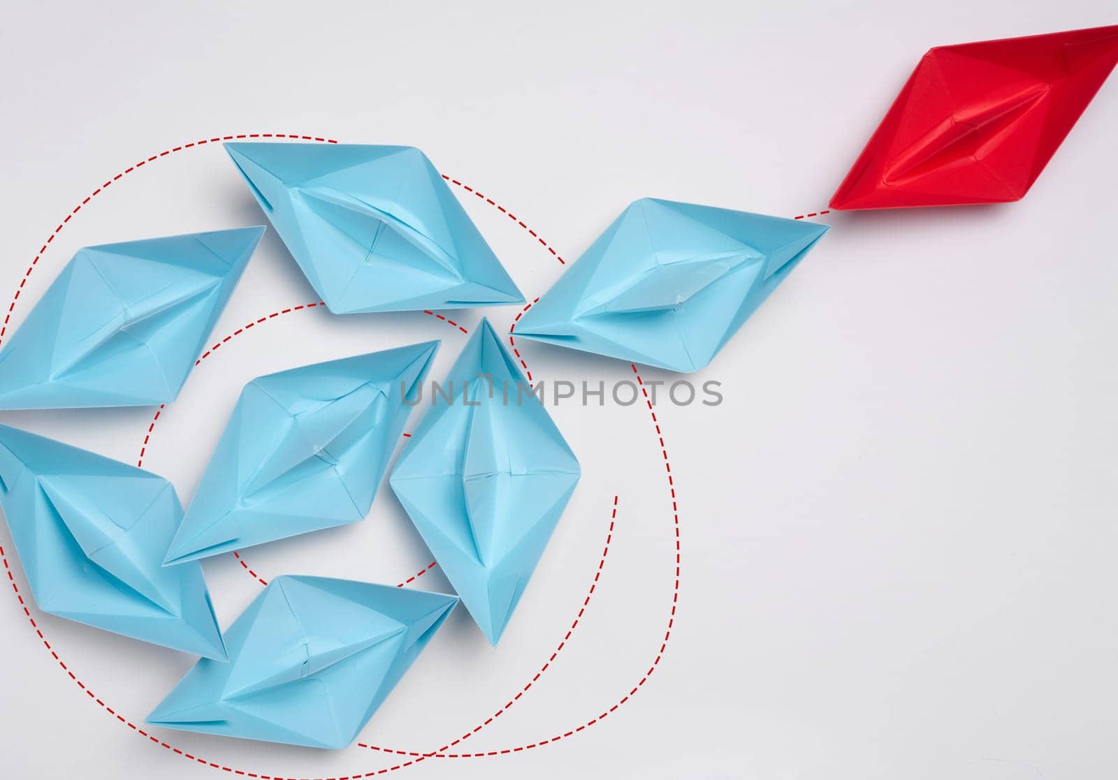 Group of blue paper boats heading in one direction and one red one heading in the opposite direction. The concept of individuality, uniqueness and talent of the employee. Get away from the influence