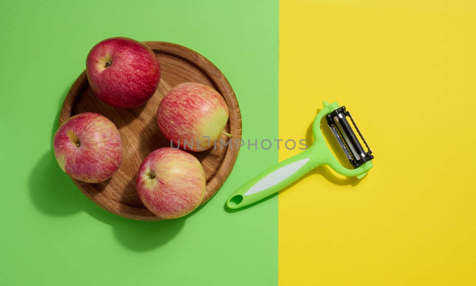 Red apples and peeler on green background, top view