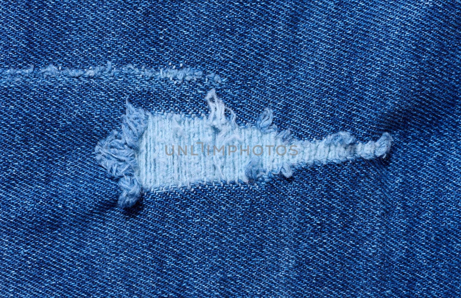 Fragment of blue jeans fabric with a hole, full frame, close up