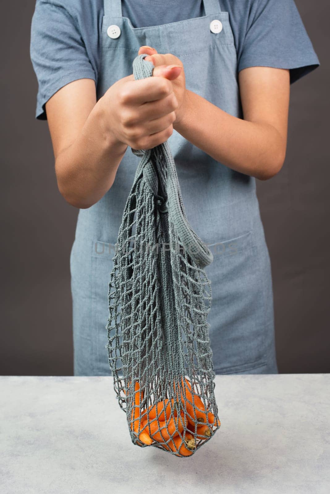Holding fresh carrots in a reusable grocery mesh bag, vegetables from the market, healthy food and zero waste